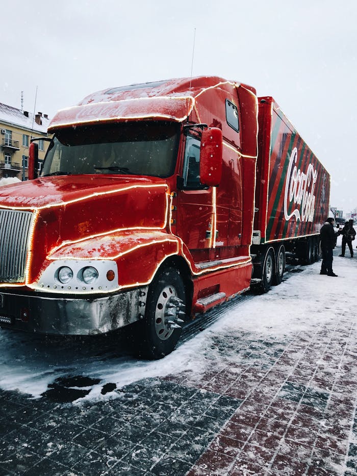 Red Coca-Cola truck parked on a snow-covered street, surrounded by people in winter.